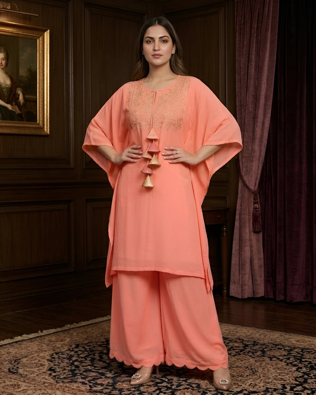Woman in a peach outfit standing in an elegant room with a painting on the wall.