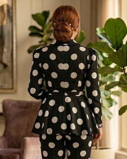 Person wearing a black polka dot outfit in a room with plants and a painting.