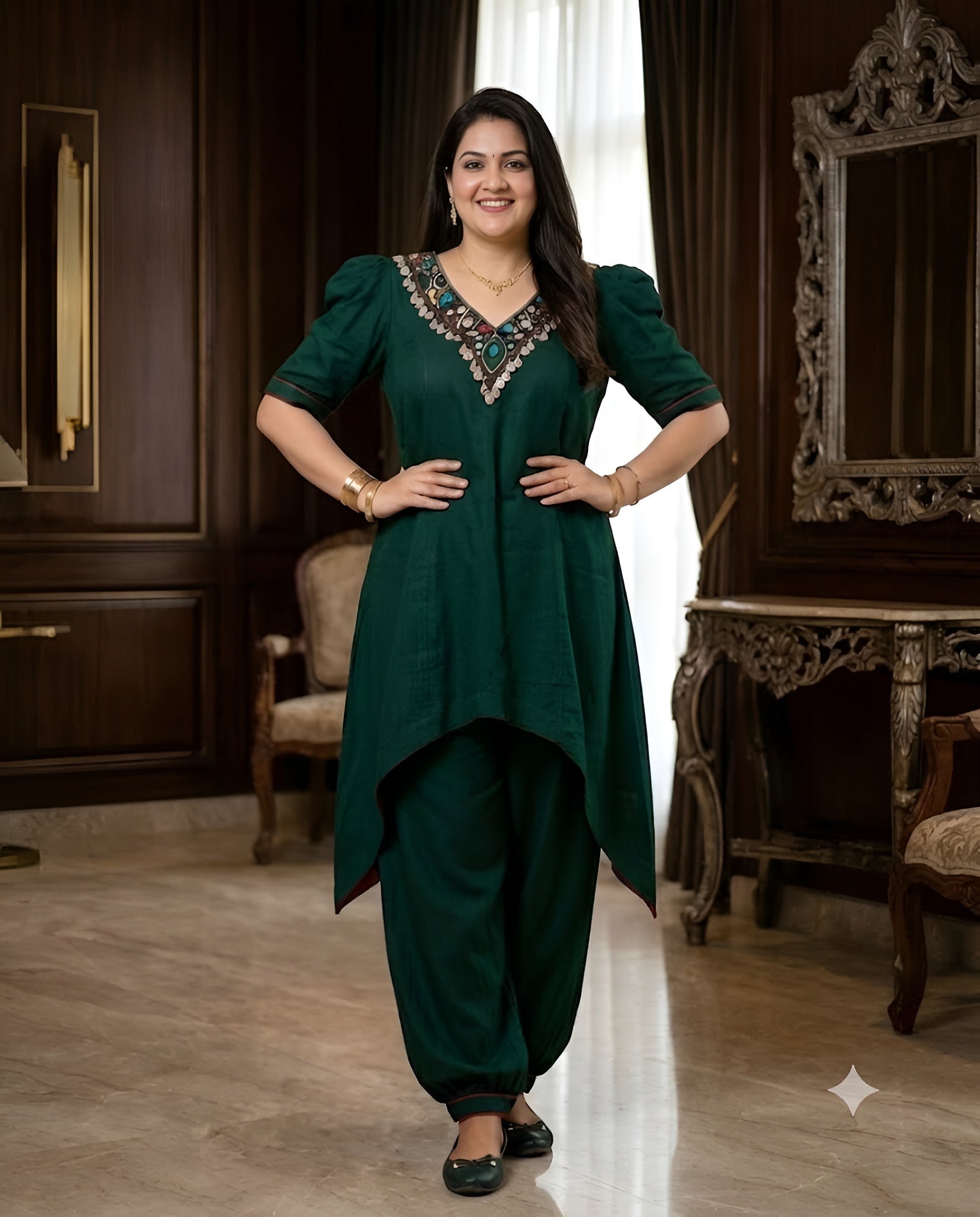 A woman modeling a dark green high-low kurta set with matching pants in an elegant, dark wood-paneled room.