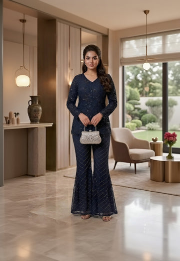 Woman in a navy blue outfit standing in a modern indoor setting with a garden view.