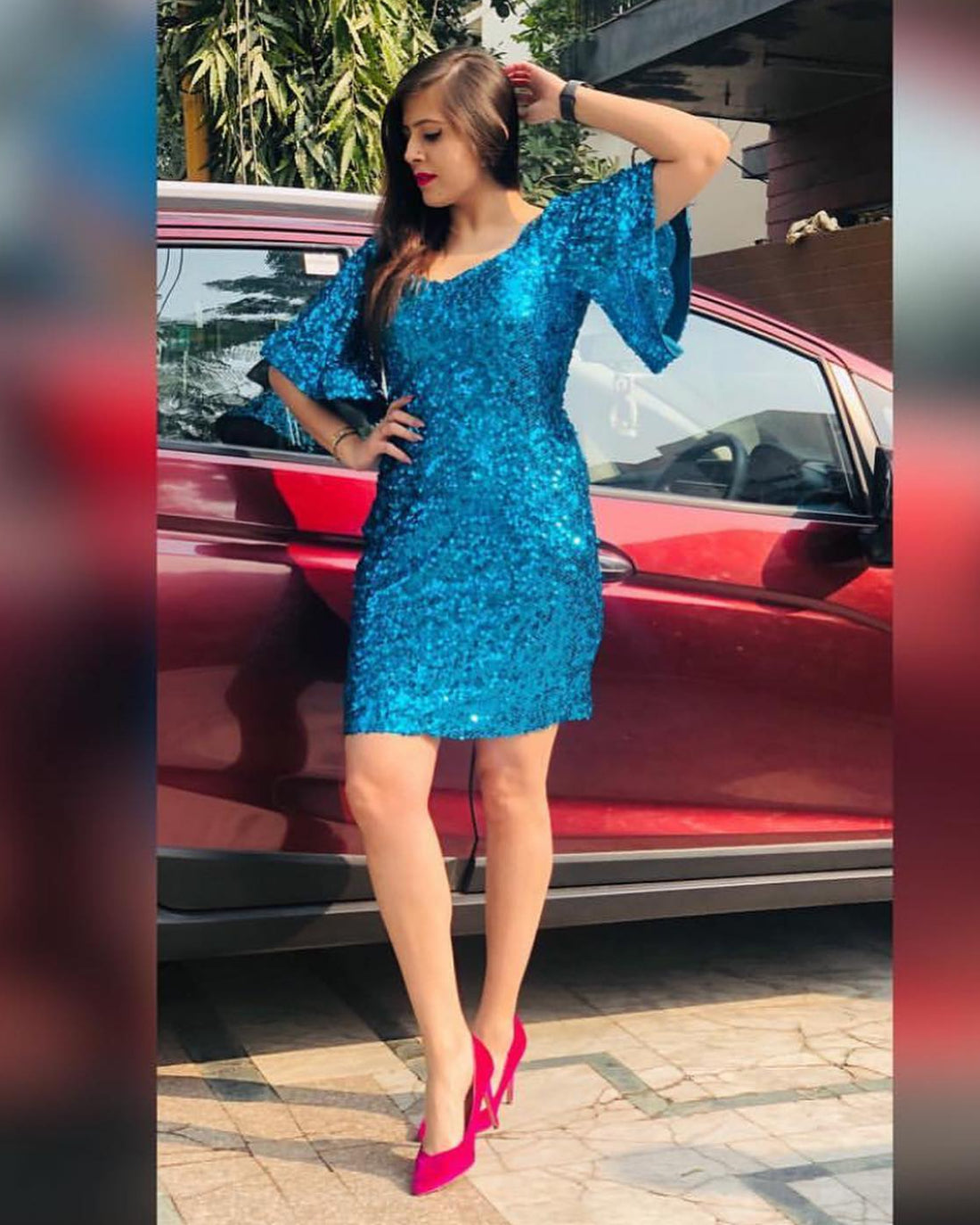 Woman in a blue dress standing next to a red car