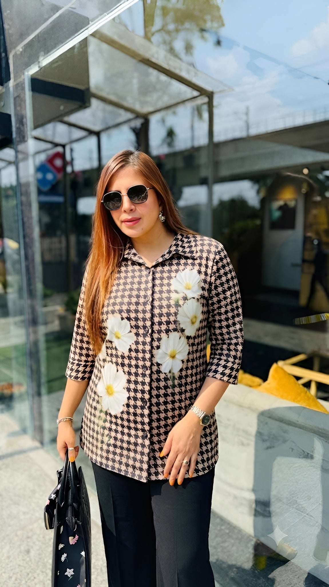 Woman wearing a checkered shirt with floral patterns outdoors.