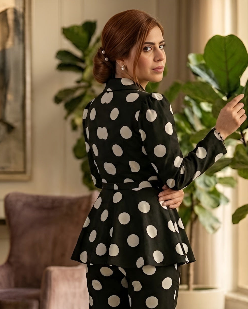 Woman in a black polka dot dress standing in a room with plants and a painting.