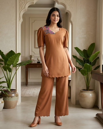 Woman in a brown outfit standing in a stylishly decorated room with plants and furniture.