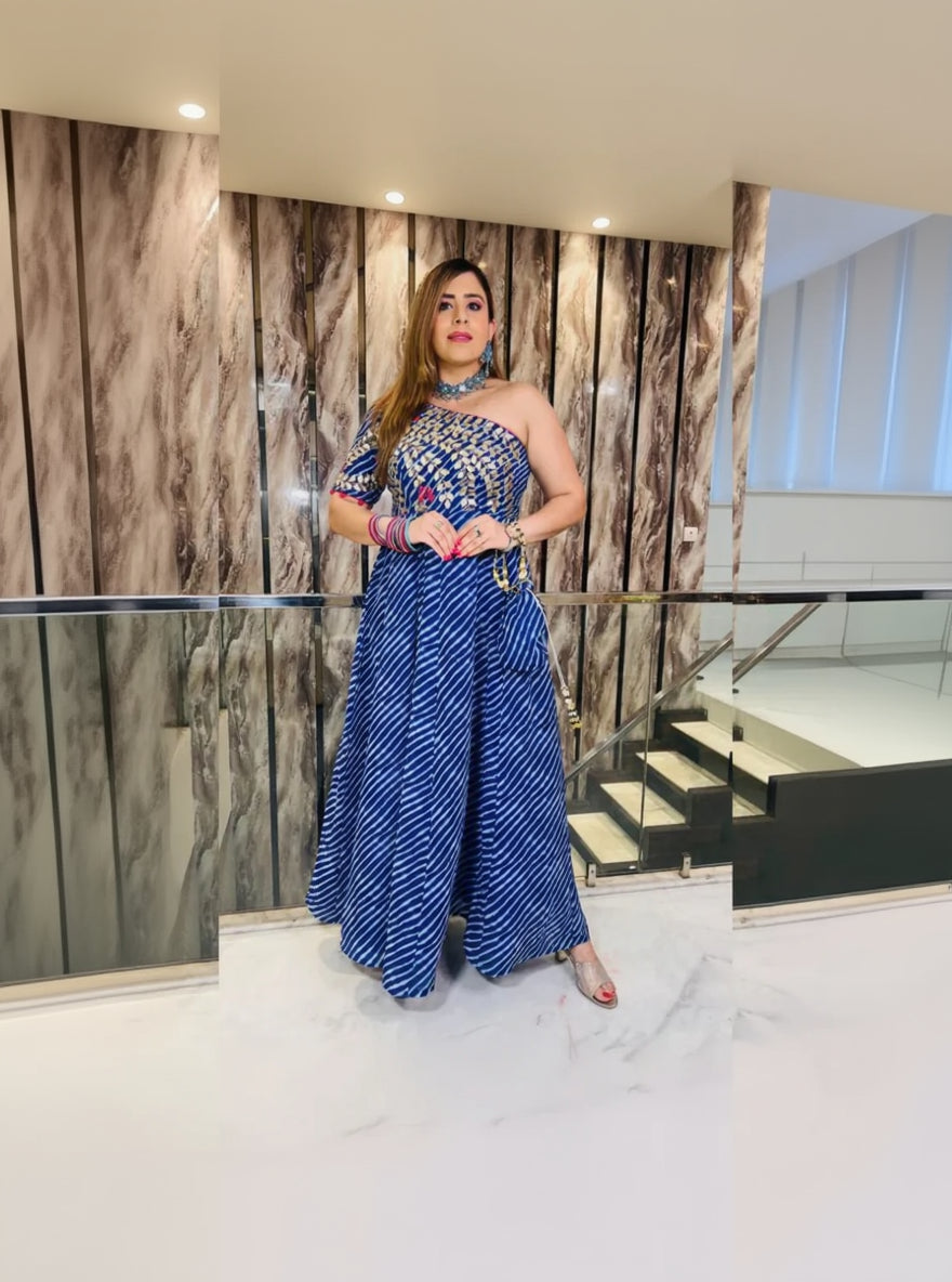 A woman wearing a traditional blue leheriya maxi with geometric patterns and embroidery, standing in a luxurious setting.