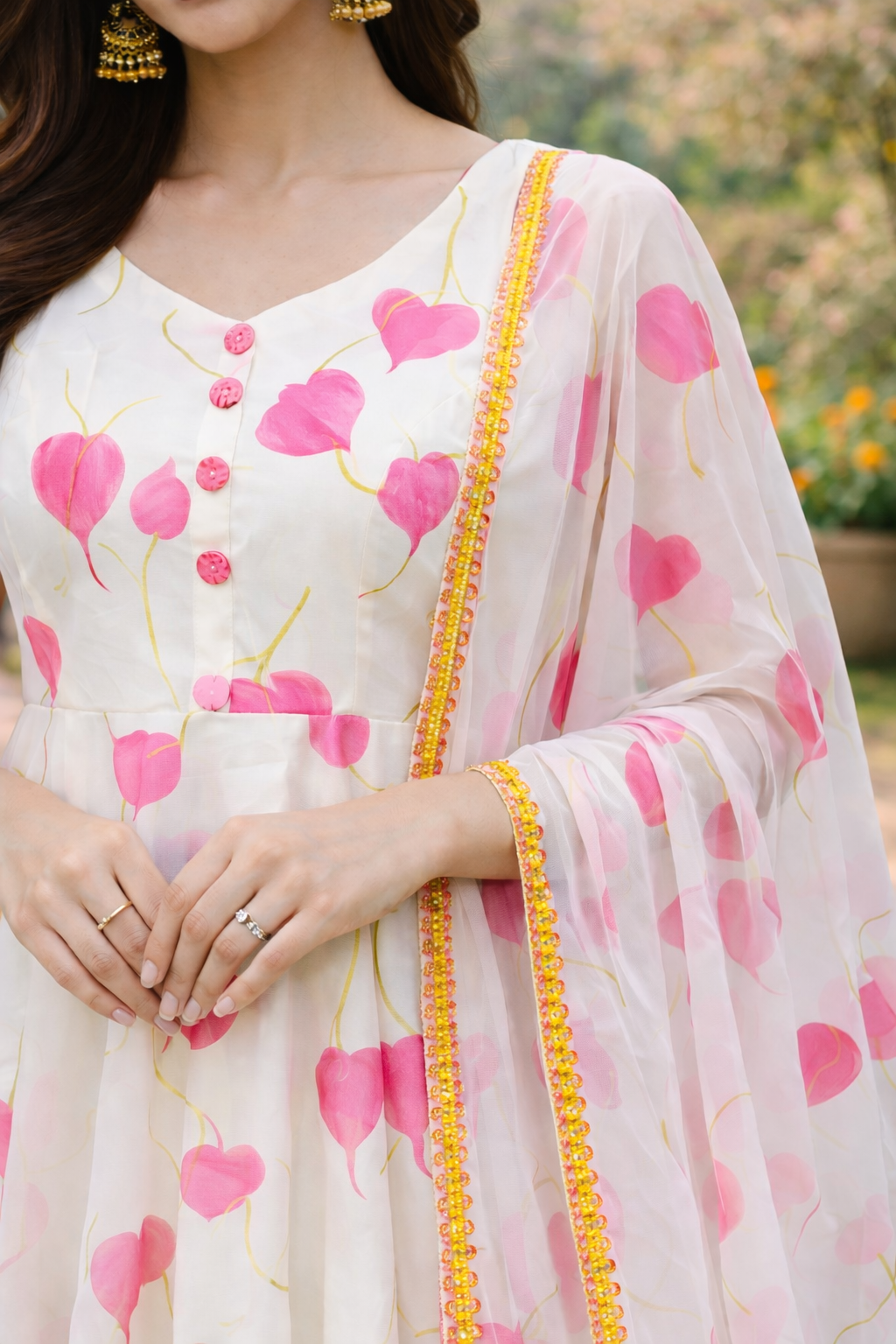 Woman in a white dress with pink floral patterns standing outdoors in a garden setting.