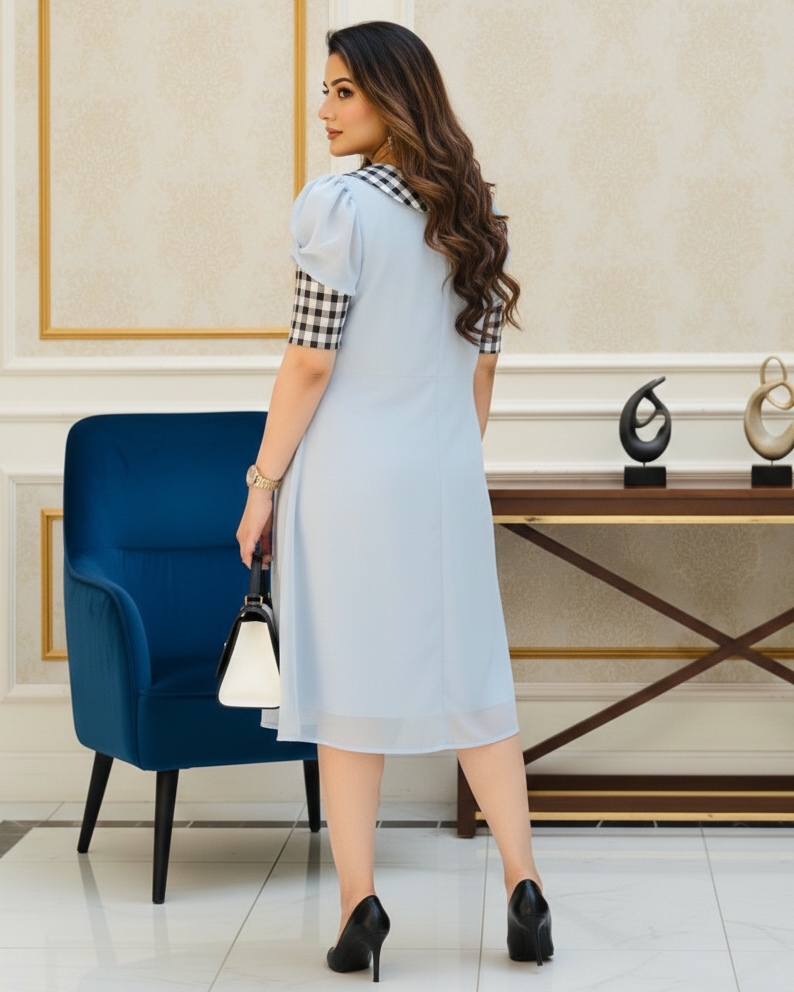 Woman in a light blue dress standing in an elegant room with a blue chair and decorative items.