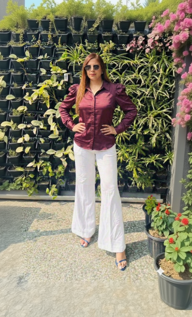 Woman wearing a maroon shirt and white pants standing in front of potted plants.