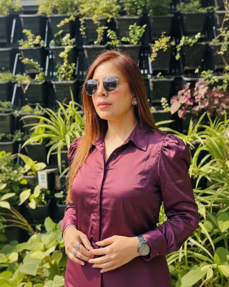 Woman wearing a purple shirt and sunglasses in front of plants