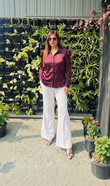 Woman in a purple shirt and white pants standing in front of potted plants