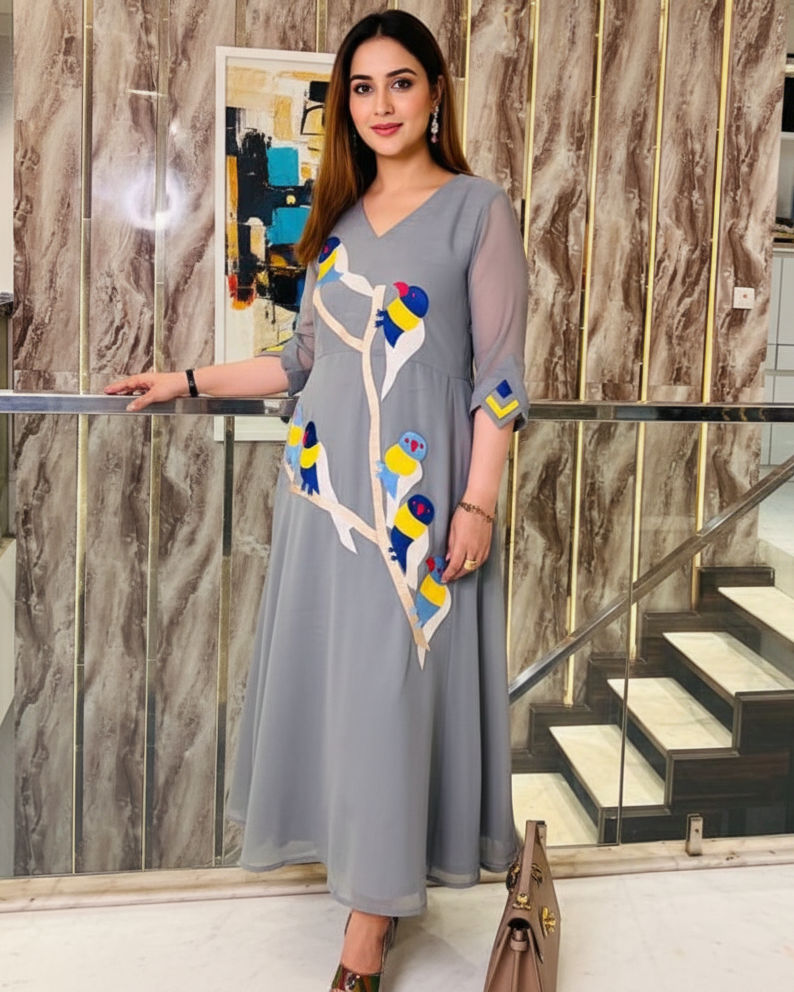 Woman in a gray dress with colorful patterns standing indoors against a marble wall.