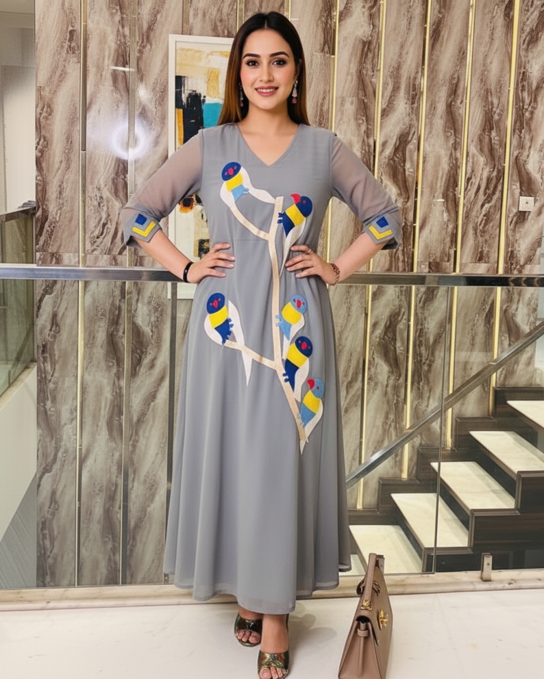 Woman in a gray dress with colorful patterns standing indoors against a marble wall.