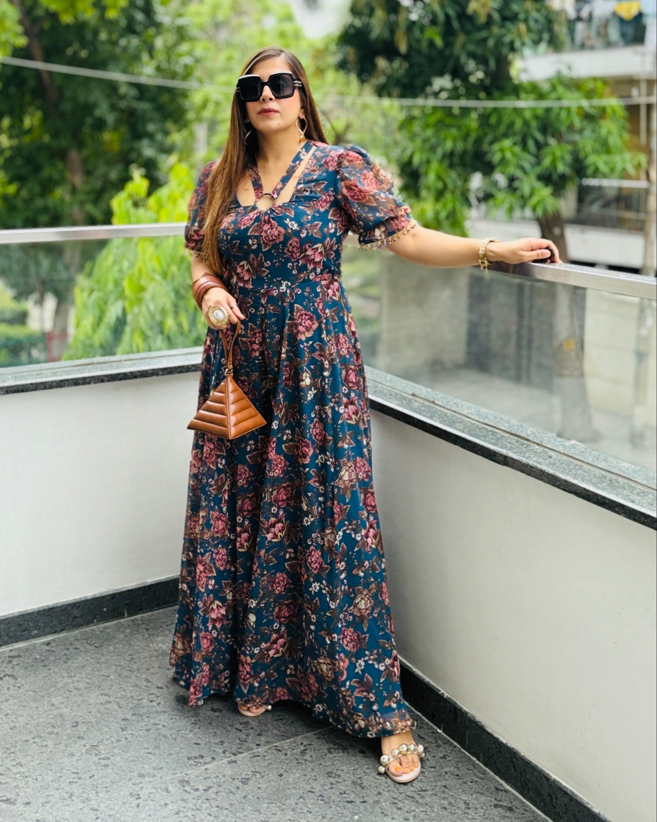 Woman in a floral dress standing on a balcony with trees in the background