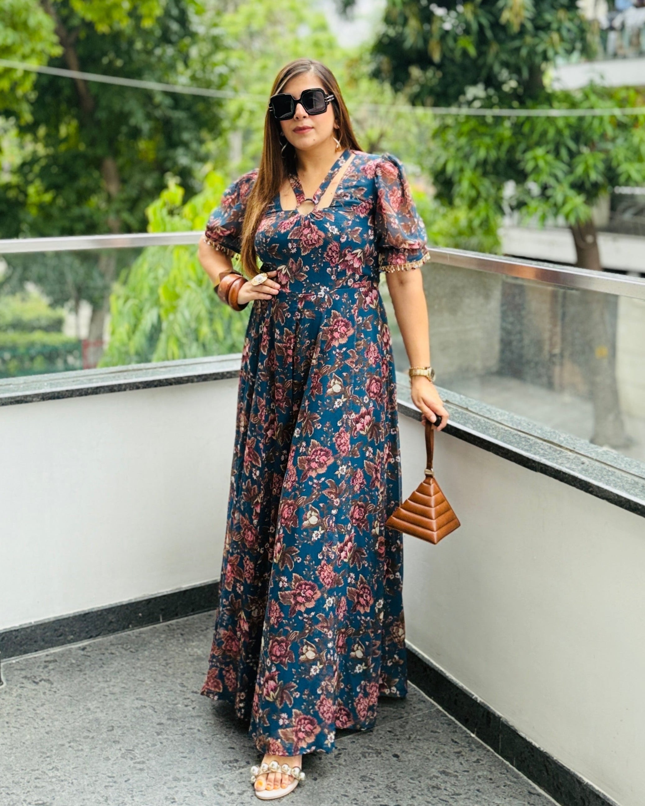 Woman in a floral dress standing on a balcony with greenery in the background