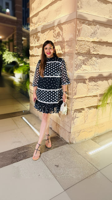 Woman in a polka dot dress standing against a stone wall at night.