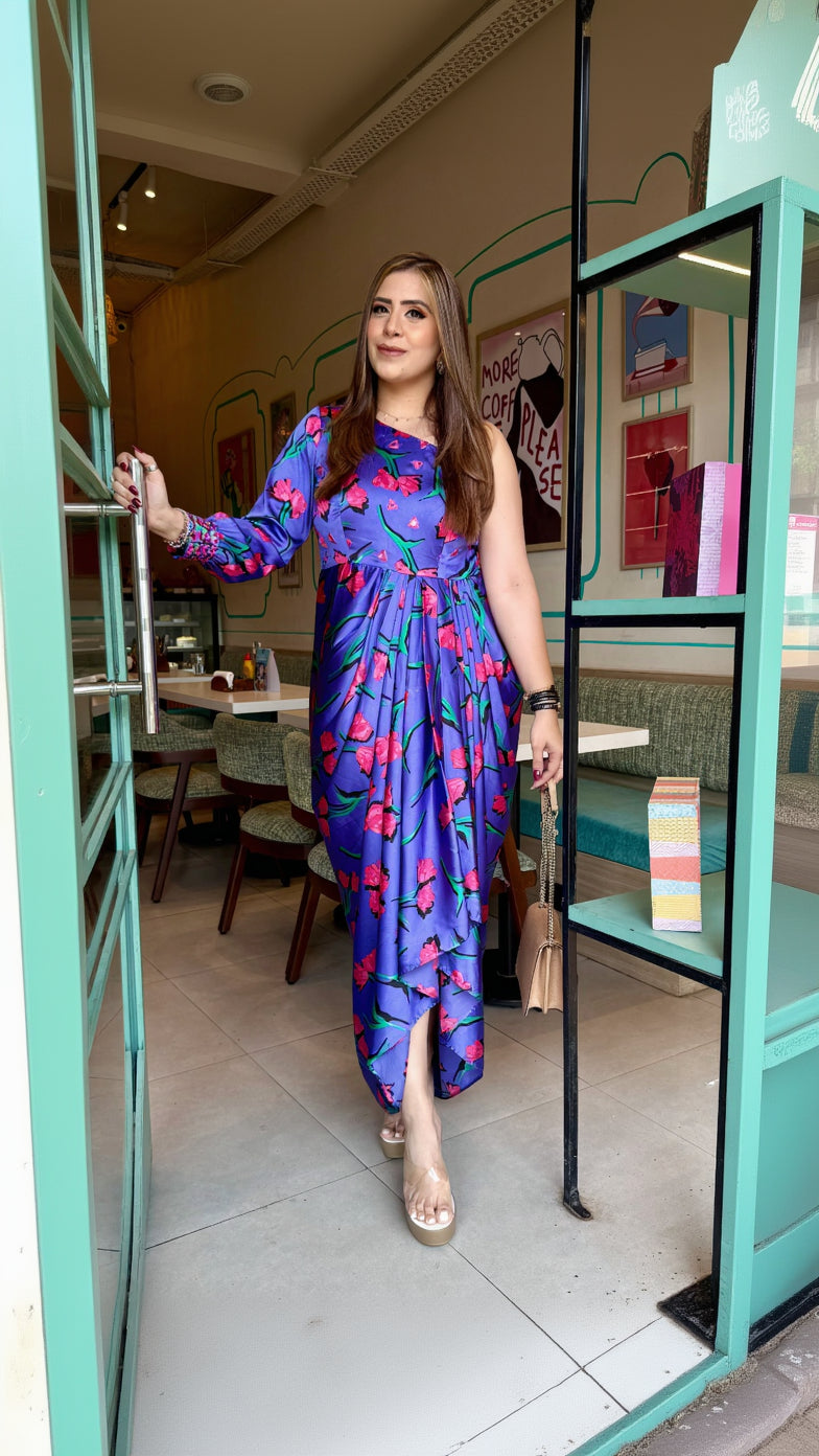 A person wearing a lavender satin drape with a one shoulder neck style and floral print, standing in a doorway.