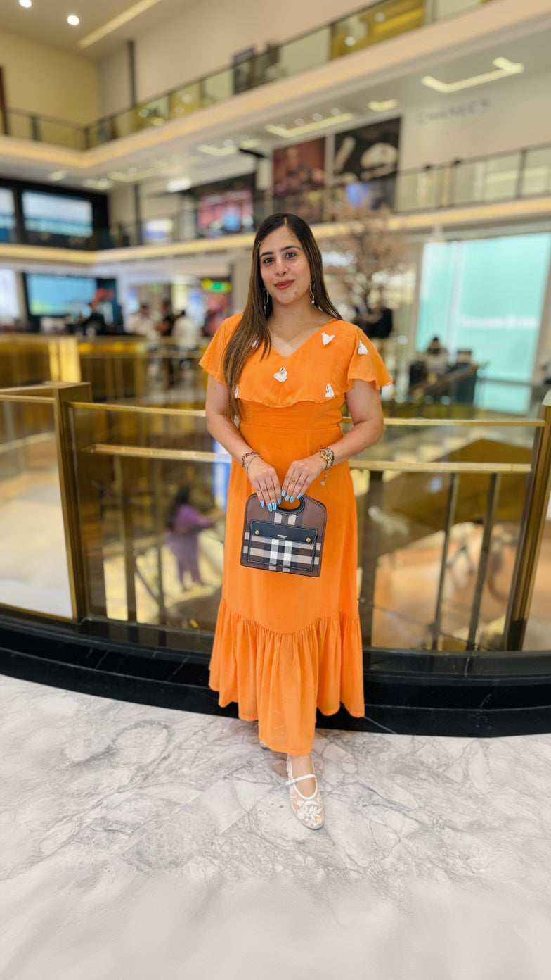Woman in an orange dress holding a small handbag in a mall setting
