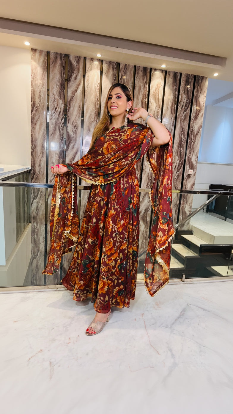A woman wearing a wine-colored, floral-patterned traditional Anarkali dress with a dupatta, holding a wine glass, and posing in a marble-themed interior.