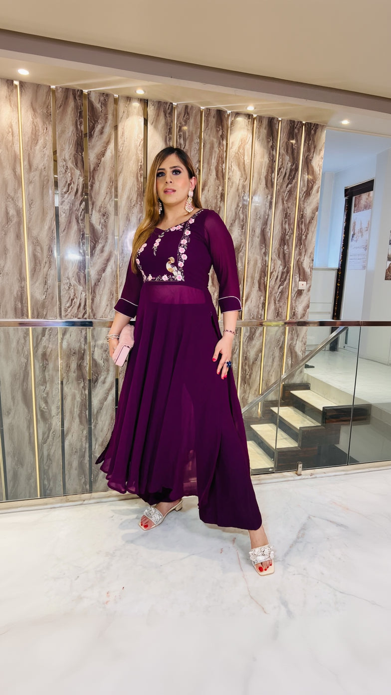A person wearing a wine-colored embroidered suit with a sweetheart neckline, 3/4th sleeves, and a flare pant with embroidery on the waist. The suit is designed for festive wear.