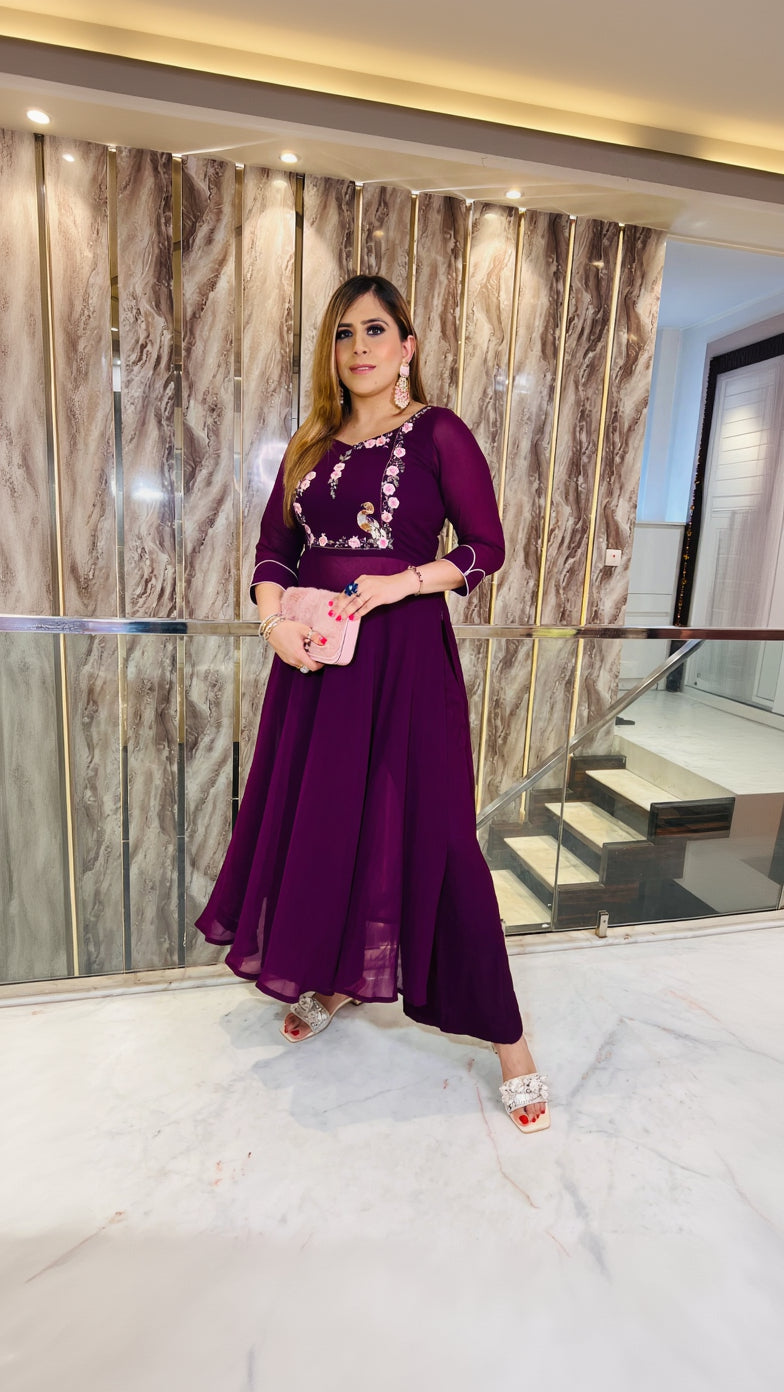 A person wearing a wine-colored embroidered suit with a sweetheart neckline, 3/4th sleeves, and a flare pant with embroidery on the waist. The suit is designed for festive wear.