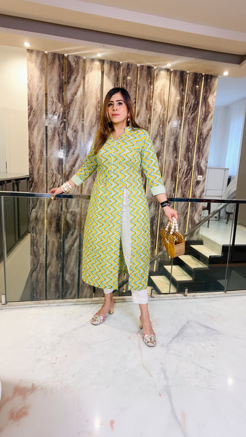 A woman wearing a pastel green, chevron patterned kurti with elbow length sleeves and a half neck cut, standing indoors with one hand on a railing.