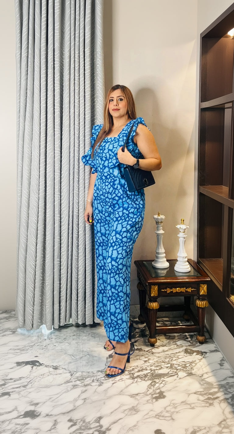 Woman in a blue patterned dress holding a blue handbag indoors.