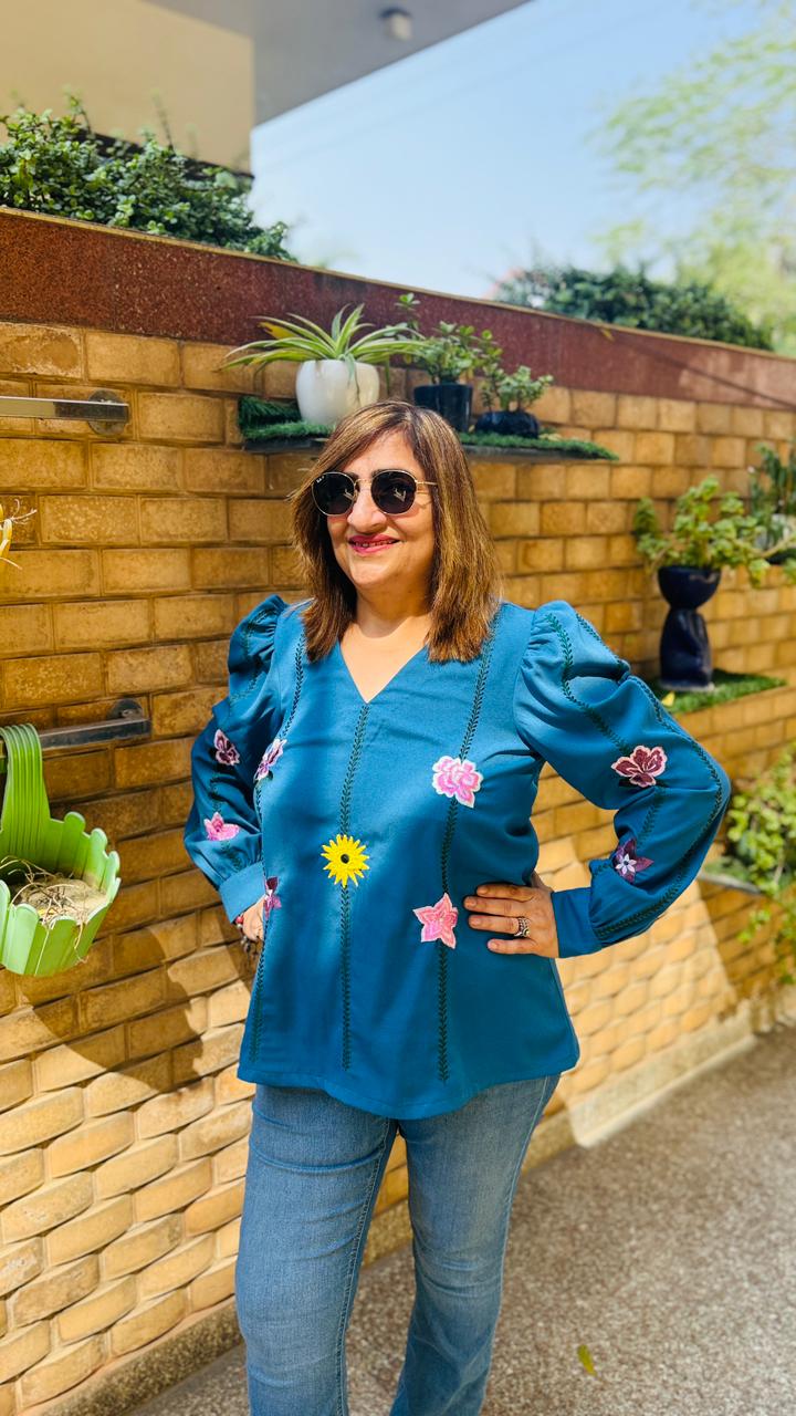 Woman in a blue jacket standing next to a wall with hanging plants on a sunny day.