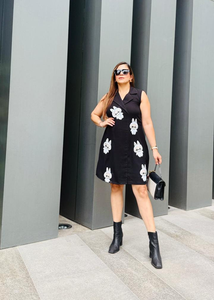 Woman in a black dress with white patterns standing in front of gray architectural columns.