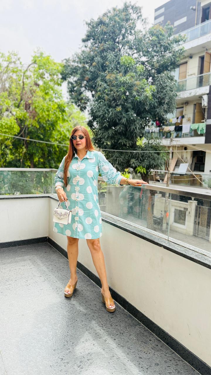 Woman in a light blue floral dress standing on a balcony with greenery in the background