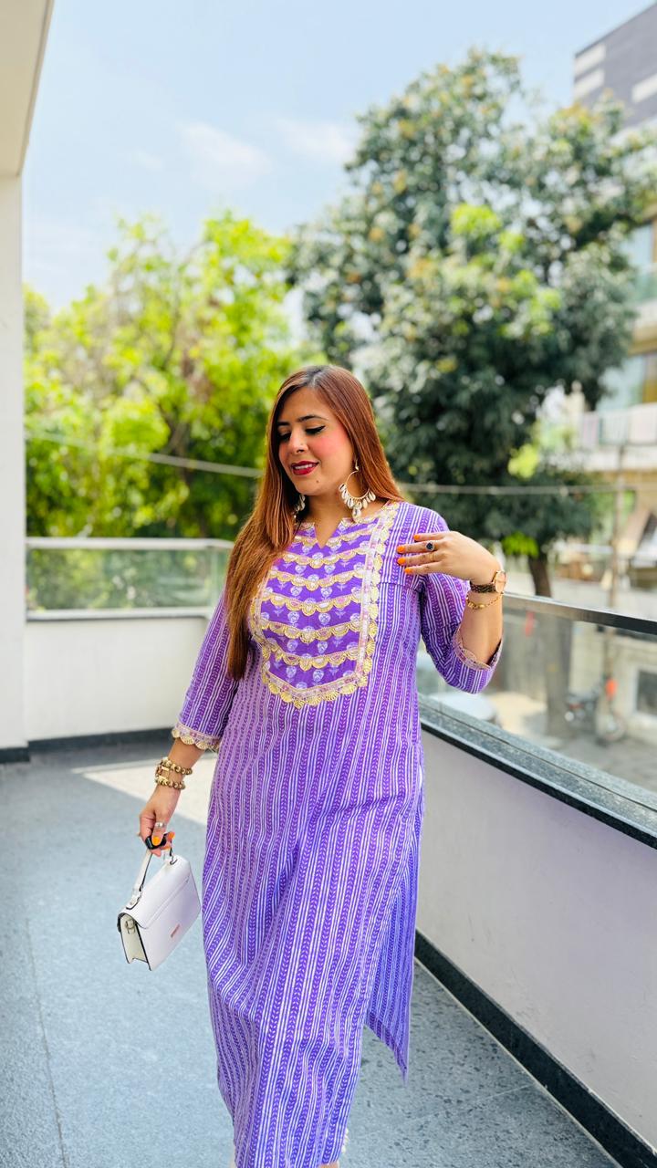 Woman in a purple outfit with white patterns standing on a balcony with greenery in the background