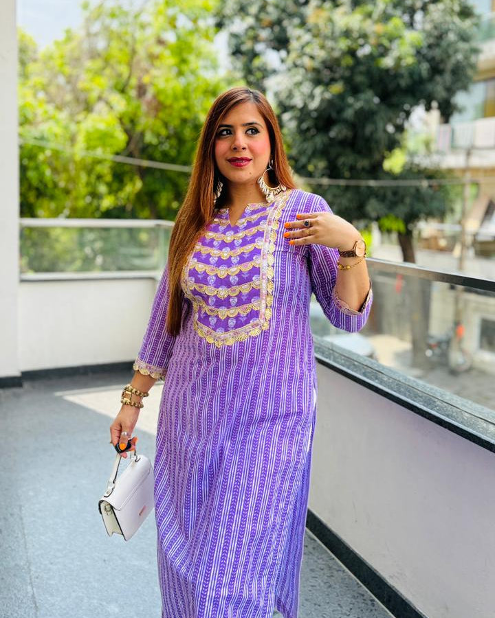 Woman in a purple dress standing on a balcony with greenery in the background