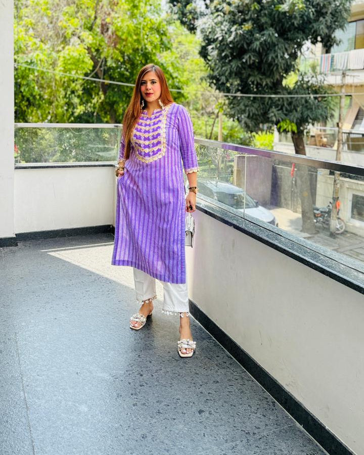 Woman in a purple dress standing on a balcony with greenery in the background