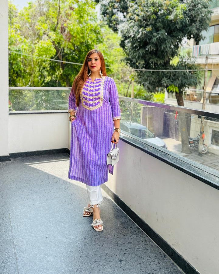 Woman in a purple dress standing on a balcony with greenery in the background