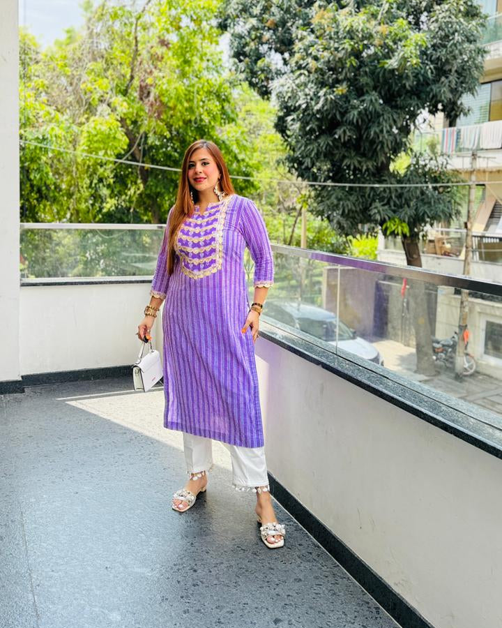 Woman in a purple traditional outfit standing on a balcony with greenery in the background