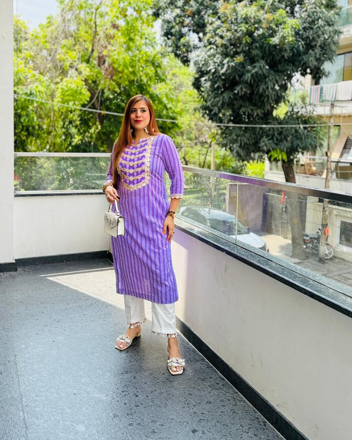 Woman in a purple traditional outfit standing on a balcony with greenery in the background