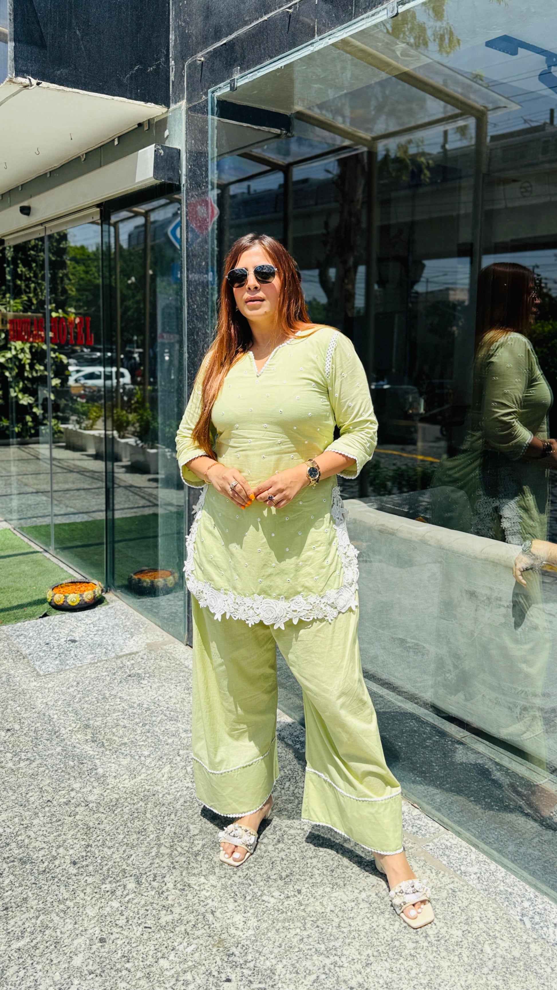 Woman in a light green outfit standing outside a building with reflective glass walls.