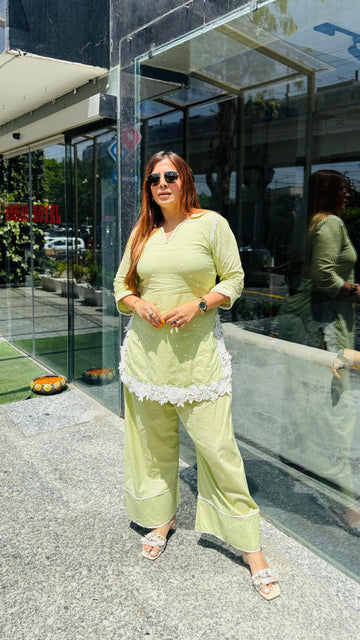Woman in a light green outfit standing outside a building with reflective glass walls.