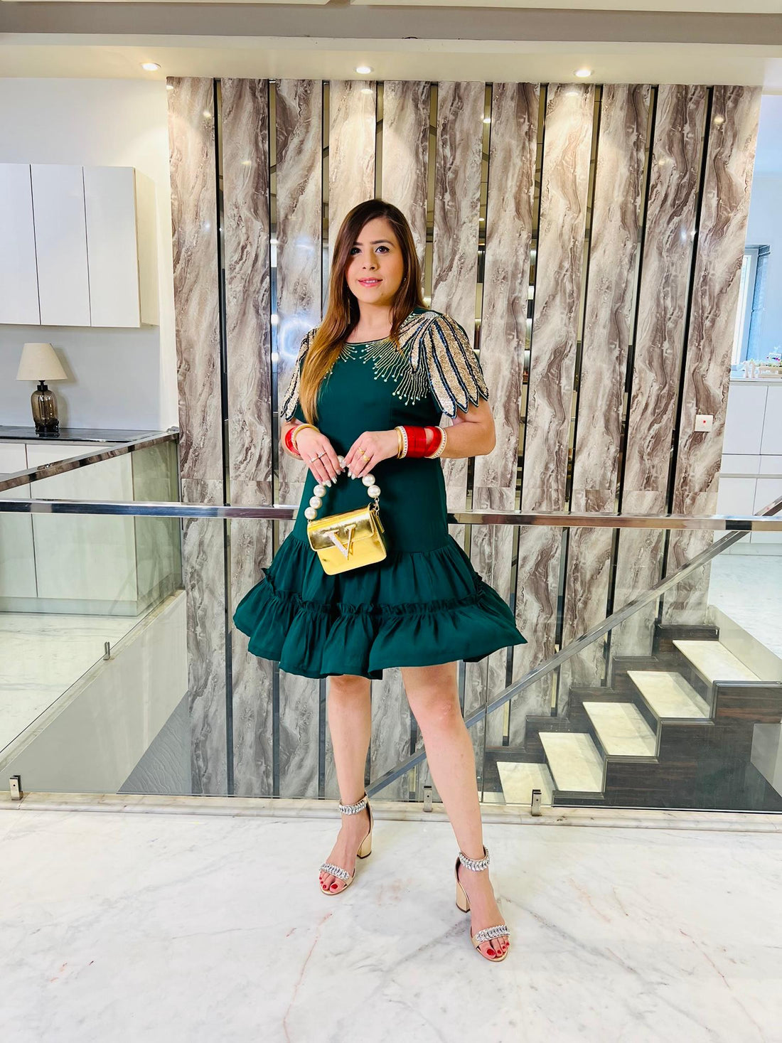 Woman in a green dress holding a gold handbag in an indoor setting with marble walls and stairs.