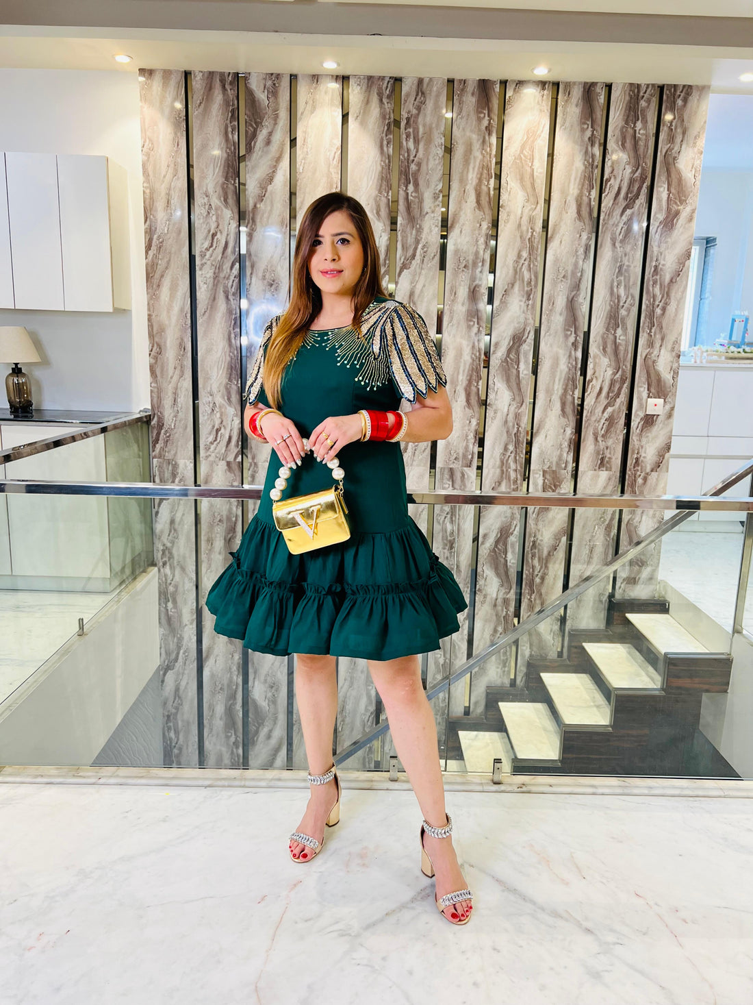 Woman in a green dress holding a gold handbag in an indoor setting with marble walls and stairs.