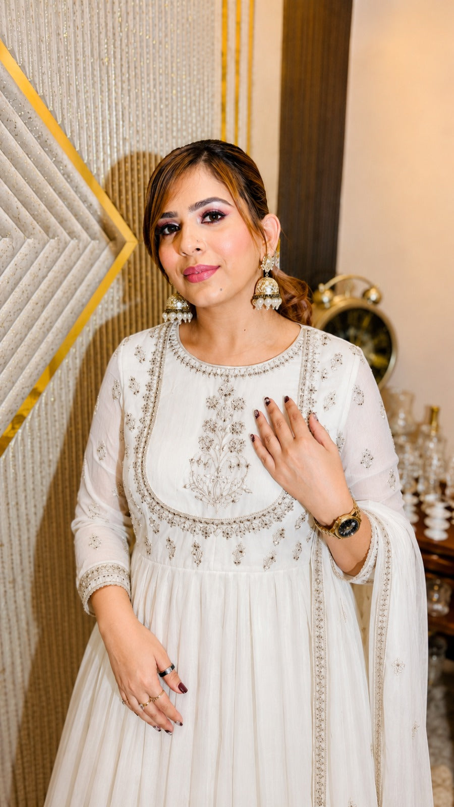 Woman in a white embroidered dress standing in an elegant interior setting.