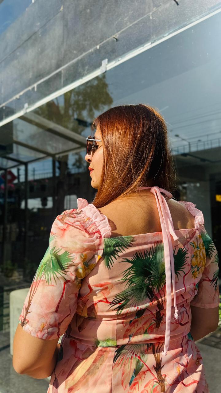 Woman wearing a floral dress with palm tree design, standing in front of a reflective surface.