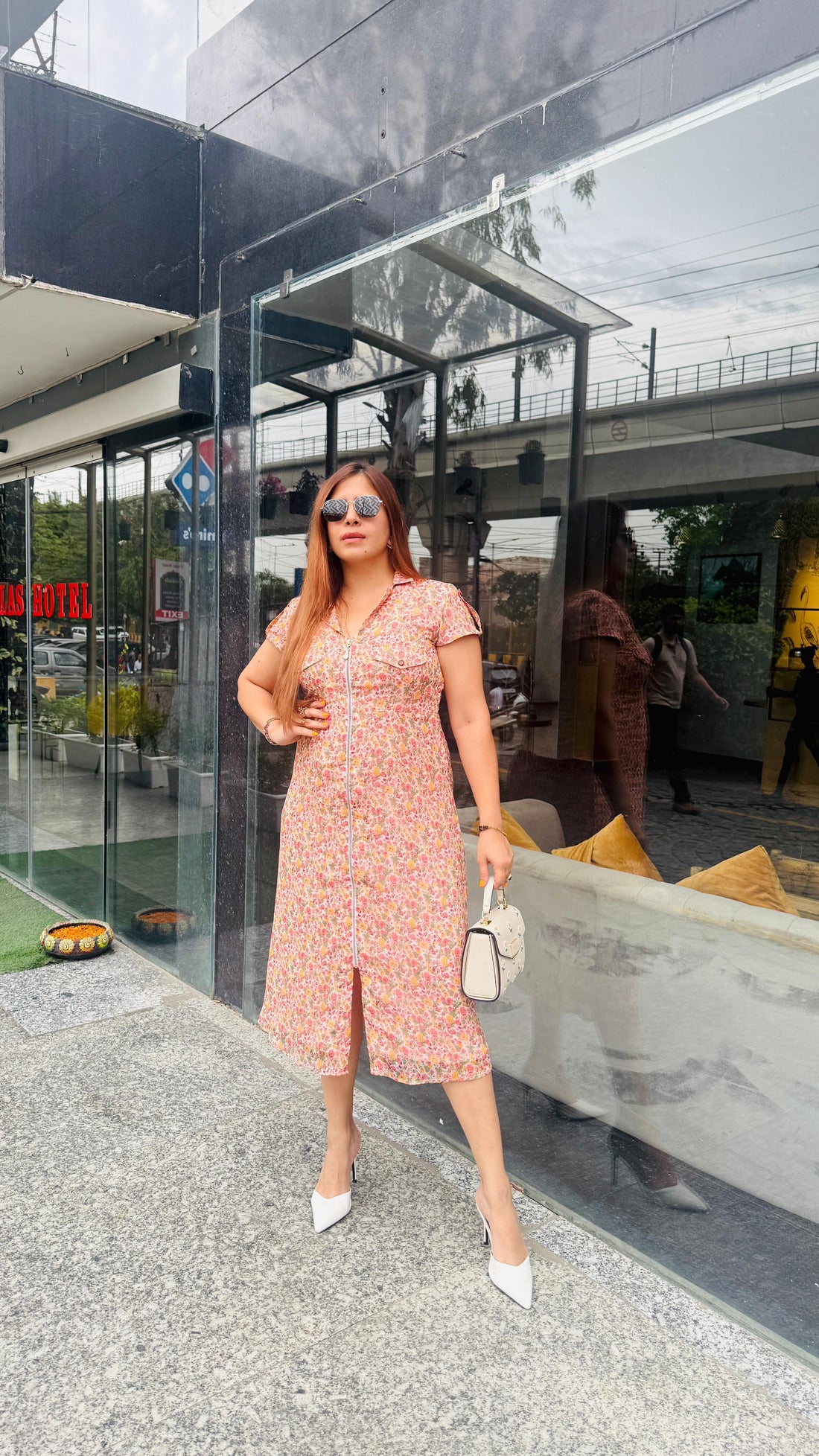 Woman in a pink dress standing in front of a modern building entrance.