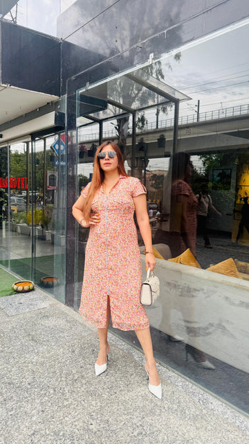 Woman in a pink dress standing in front of a modern building entrance.