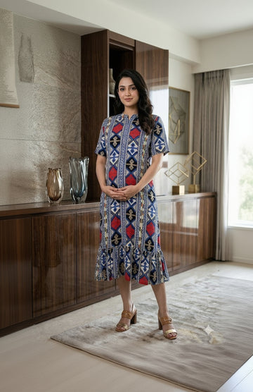 Woman wearing a patterned dress standing in an indoor setting with decor elements.