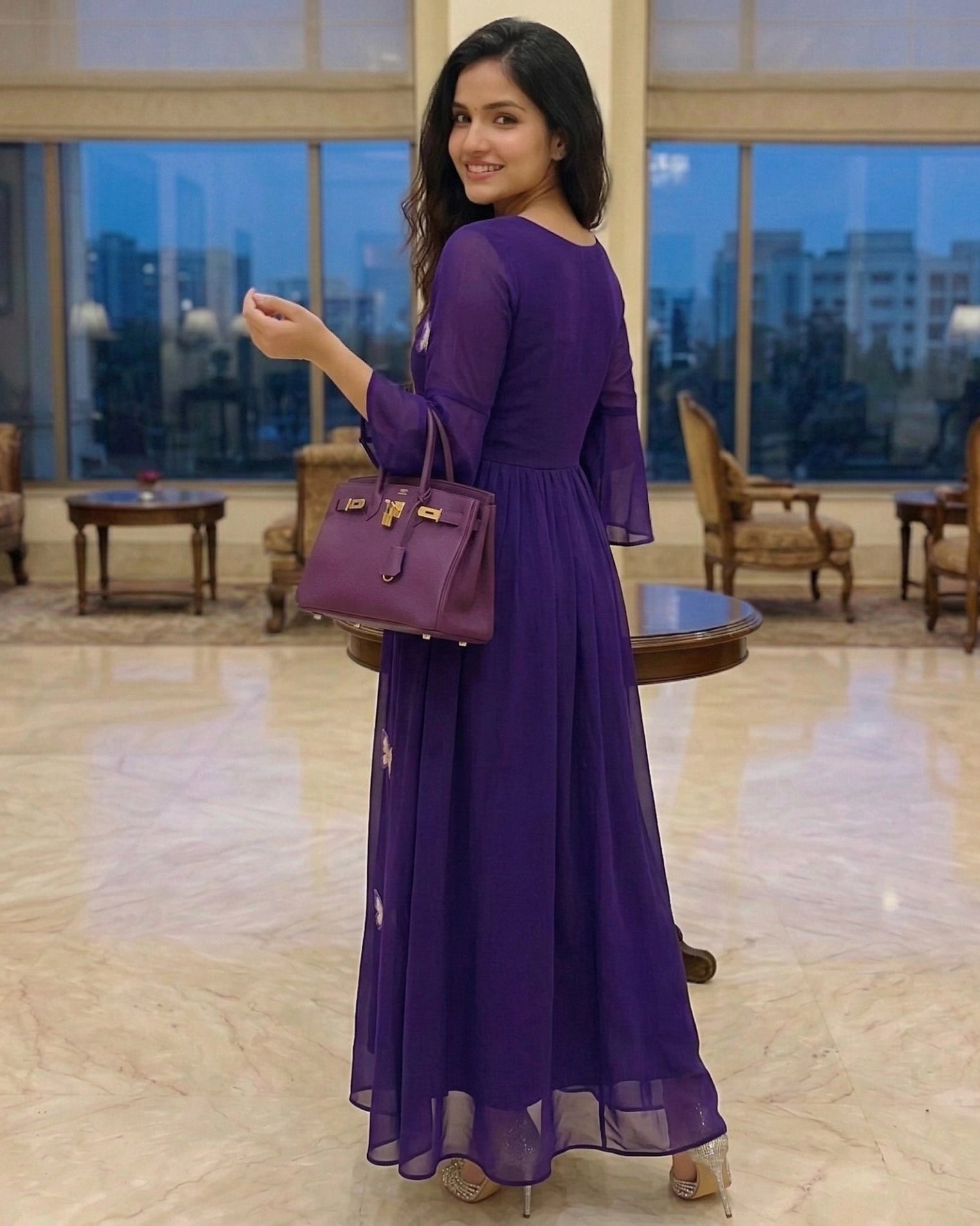 Woman in a purple dress holding a matching handbag in a luxurious room.