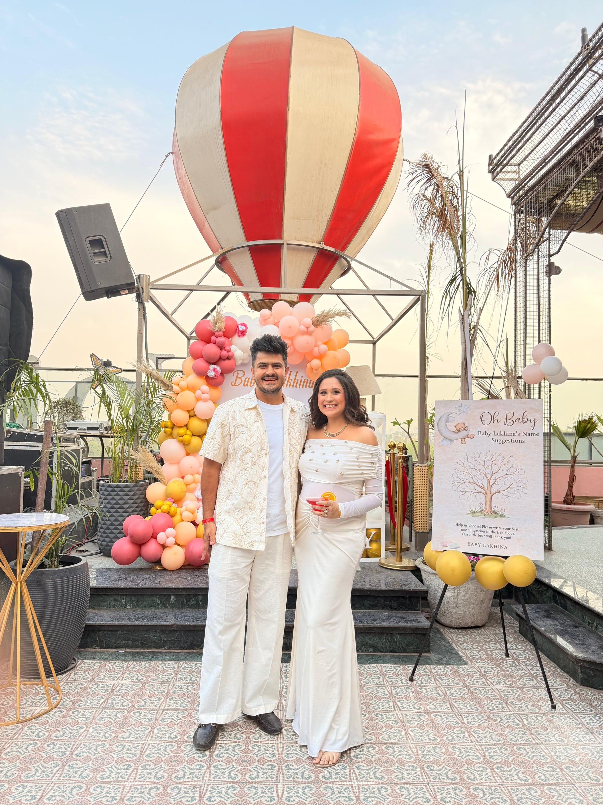 Two people standing in front of a colorful balloon display on a rooftop.