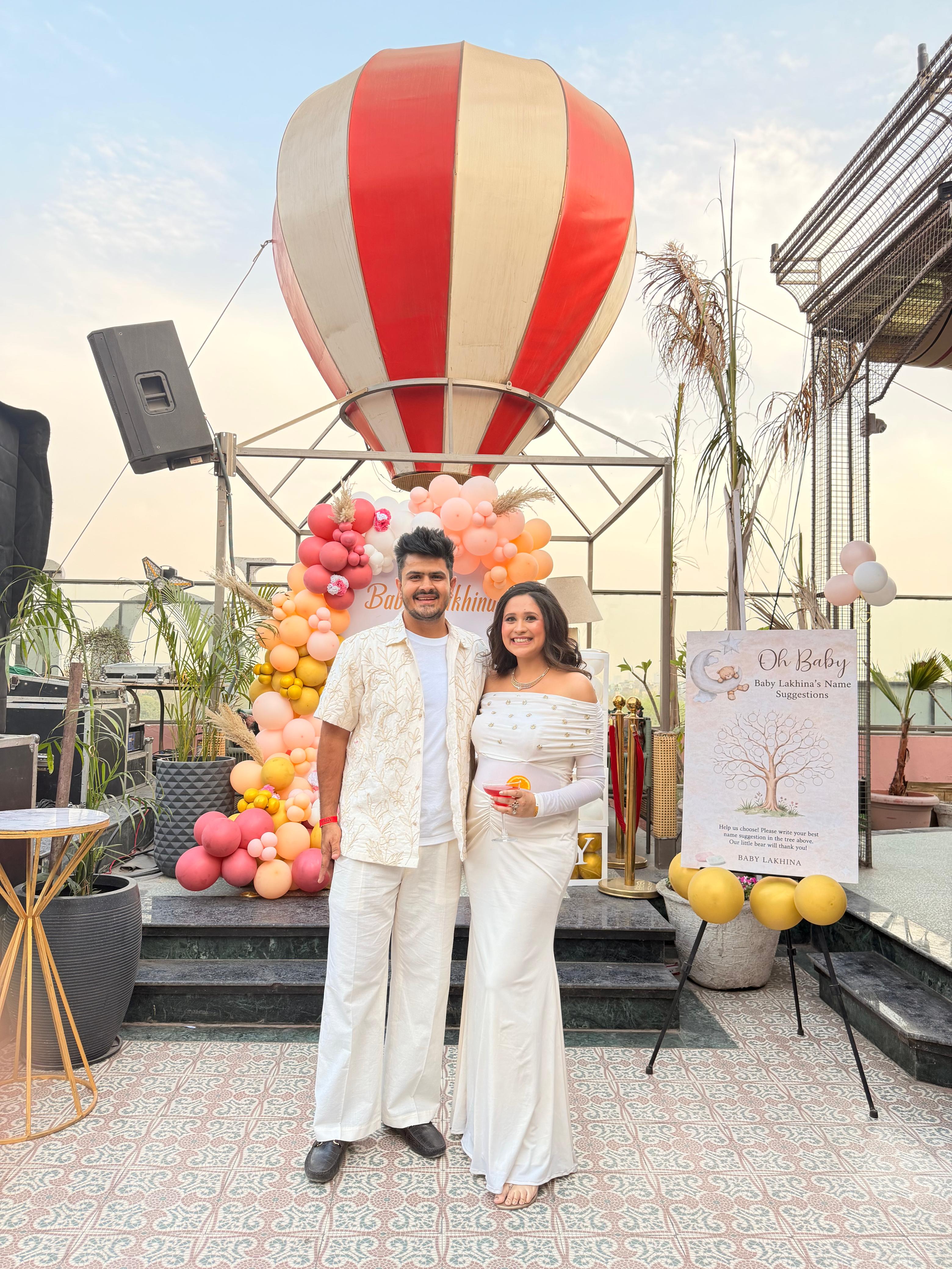 Two people standing in front of a colorful balloon display on a rooftop.