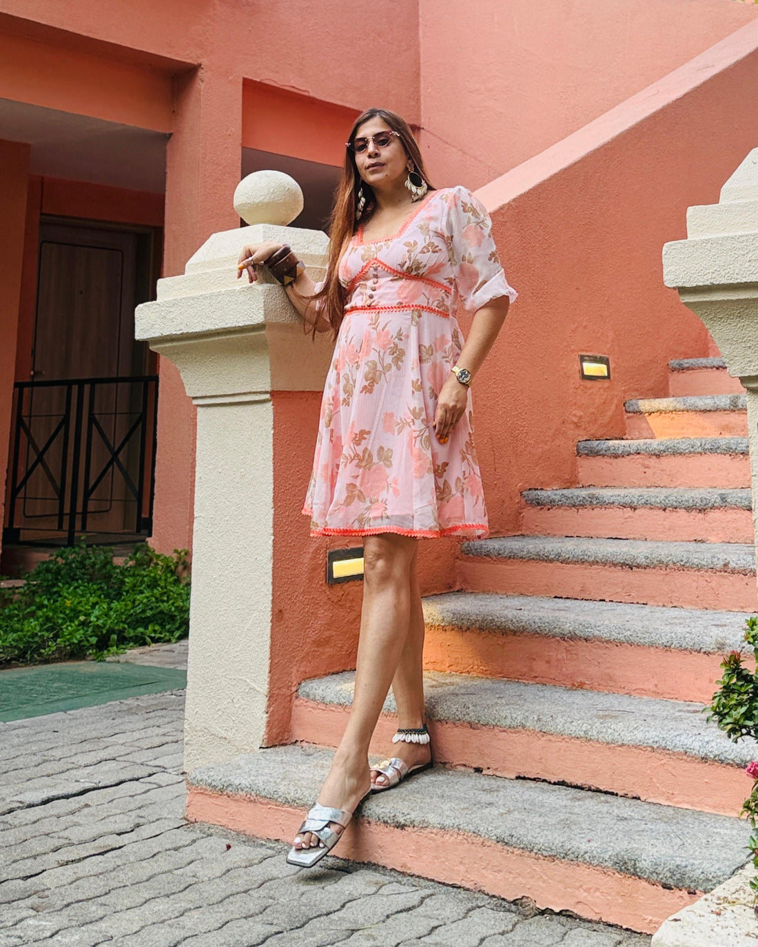 Woman in a floral dress standing on a set of stairs with a pink building in the background