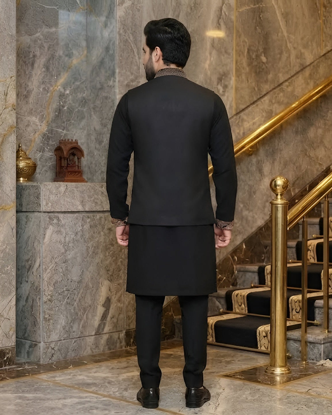 Man in a black suit standing in a luxurious interior setting with marble walls and gold accents.