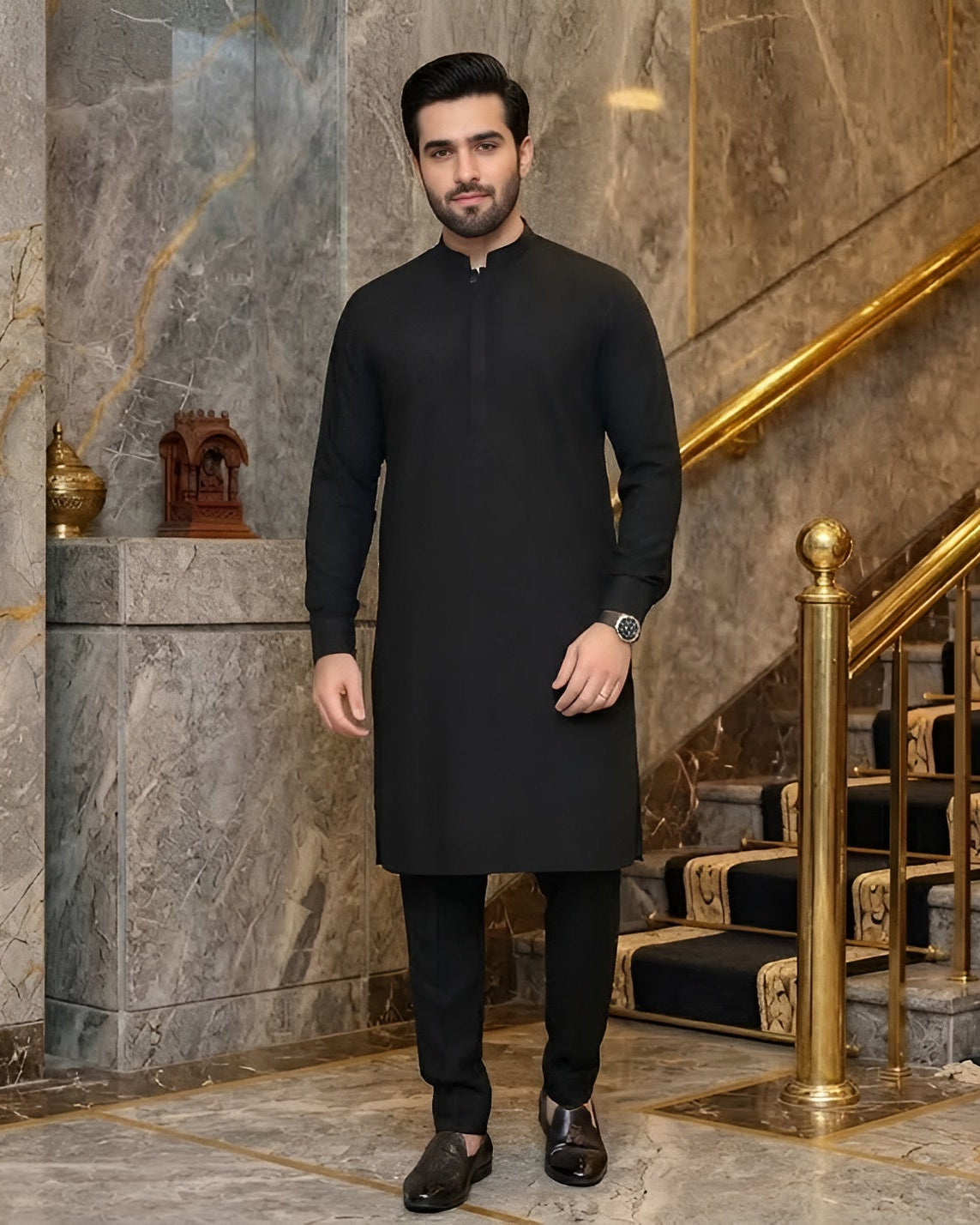 Man in a black traditional outfit standing in a luxurious interior setting with marble walls and gold accents.